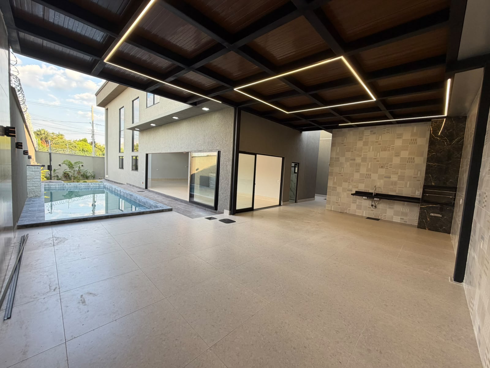 Área gourmet coberta integrada à piscina, com churrasqueira e forro de madeira